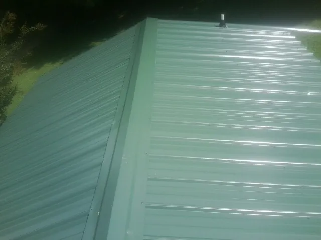 New green metal panels meeting at the ridge of a roof — Flat Roof Repair work by our crew in Bensalem