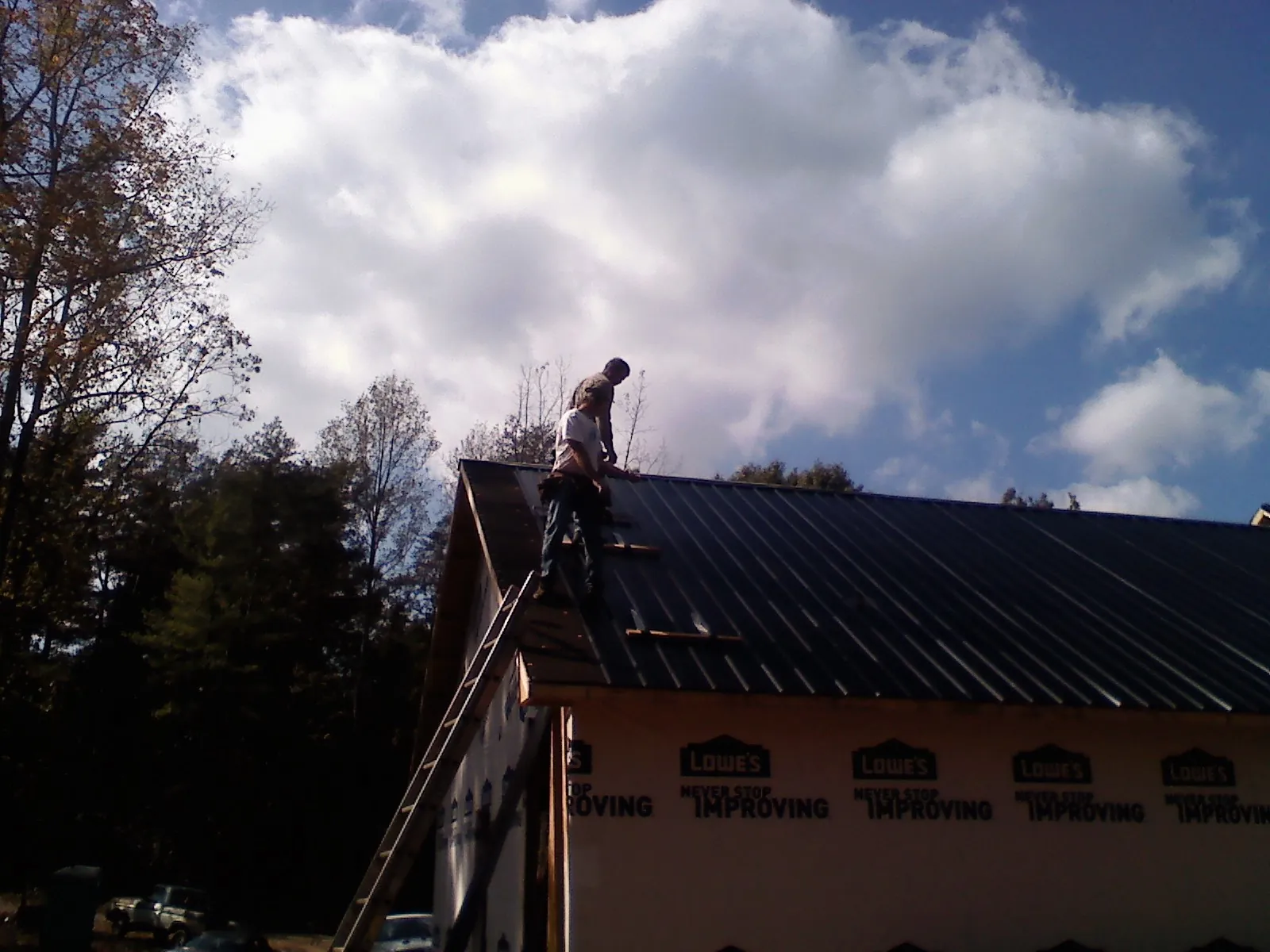 Roofer fastening dark metal panels high against a cloudy sky, from a Roof Inspection job in Bensalem