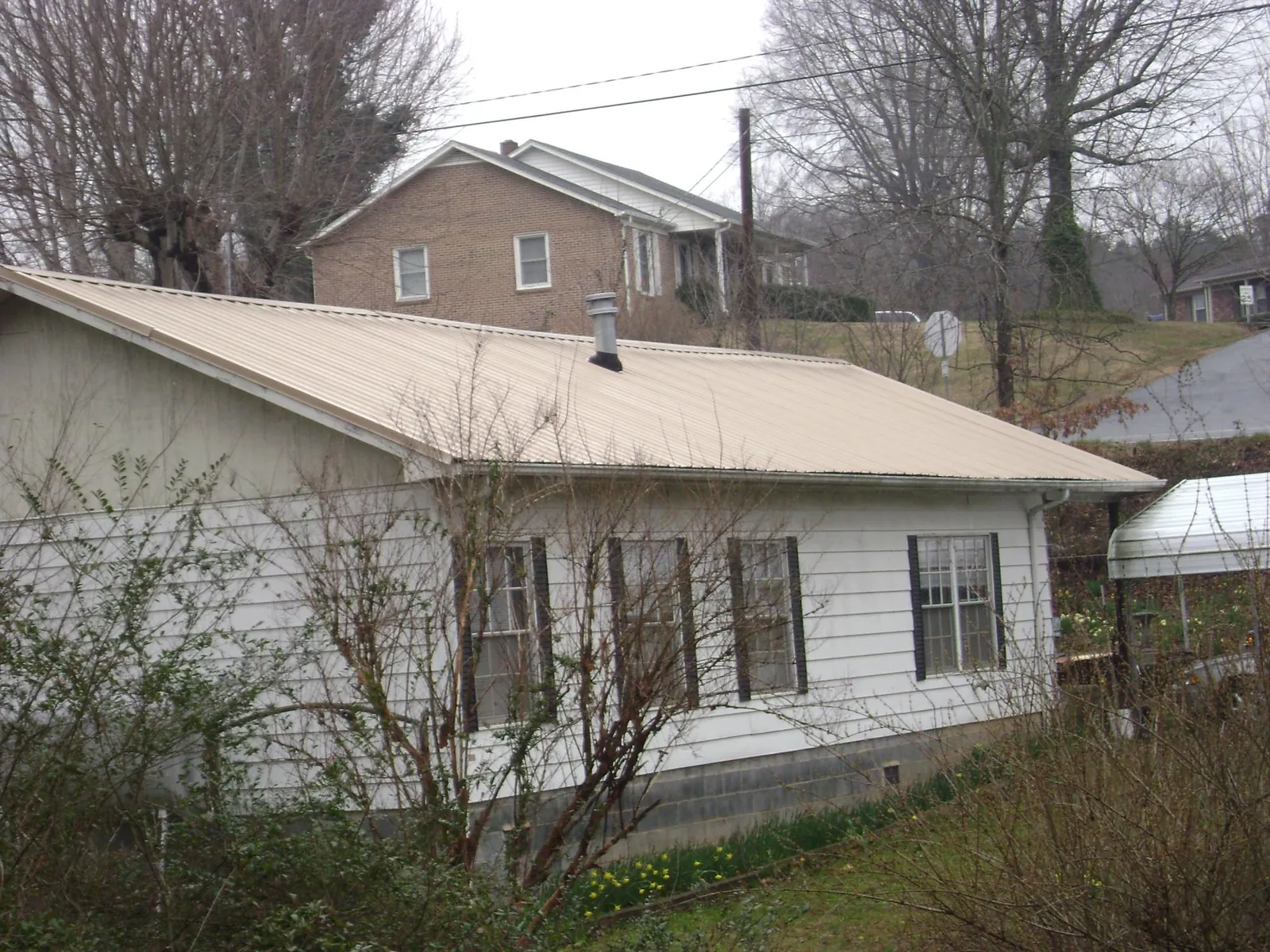 Tan metal roof on a white sided house set into a hillside — Commercial Roofing by Roofing Brothers in Bensalem